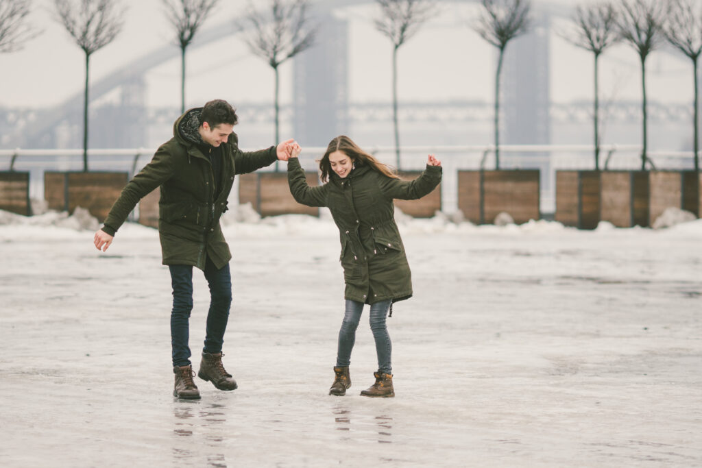 Couple holding hands and laughing while balancing on ice, symbolizing trust, communication, and connection through relationship therapy at The Mindful Place in Ontario.