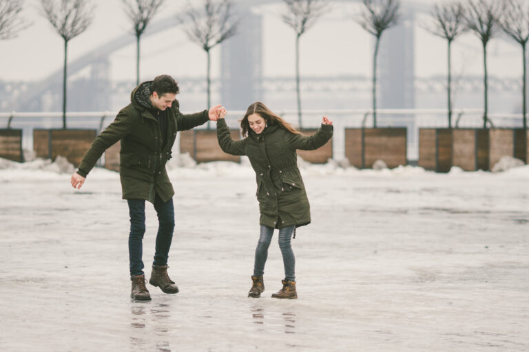 Couple holding hands and laughing while balancing on ice, symbolizing trust, communication, and connection through relationship therapy at The Mindful Place in Ontario.