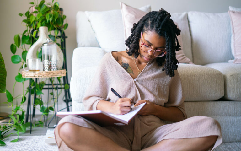 A woman sits peacefully on the floor journaling in a calm home space, practicing mindfulness and self-reflection to support emotional regulation.
