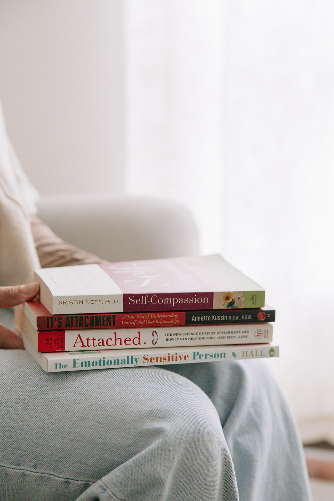 Person holding a stack of self-help and mindfulness books, representing personal growth and the practice of self-compassion as explored in The Mindful Place’s presentations in Ontario.