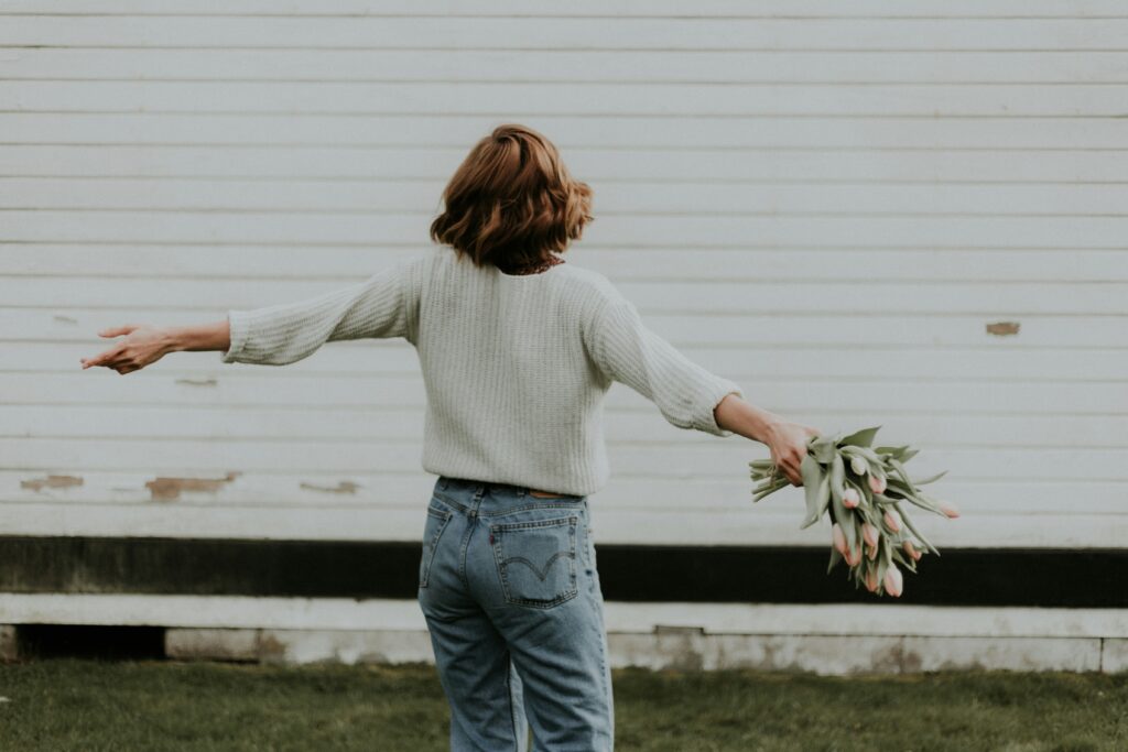 Person standing freely with open arms holding flowers, symbolizing self-acceptance and relief after overcoming people-pleasing patterns through therapy at The Mindful Place in Ontario.