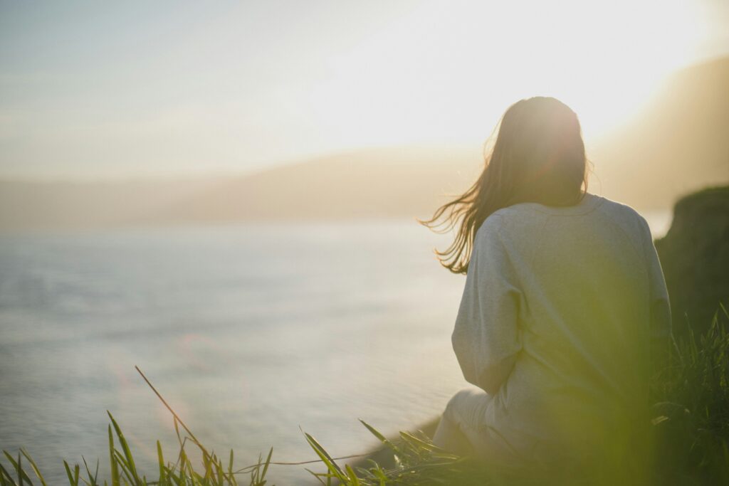 Person sitting peacefully by the water at sunrise, representing calm, balance, and mindfulness achieved through stress management therapy at The Mindful Place in Ontario.
