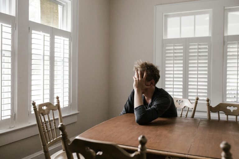 A person sitting at a table with their head in their hand, representing feelings of stress and overwhelm before learning healthy coping strategies.