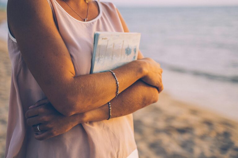 Person gently holding a journal close to their chest on a beach, symbolizing self-reflection, care, and the practice of self-compassion, at The Mindful Place in Ontario.