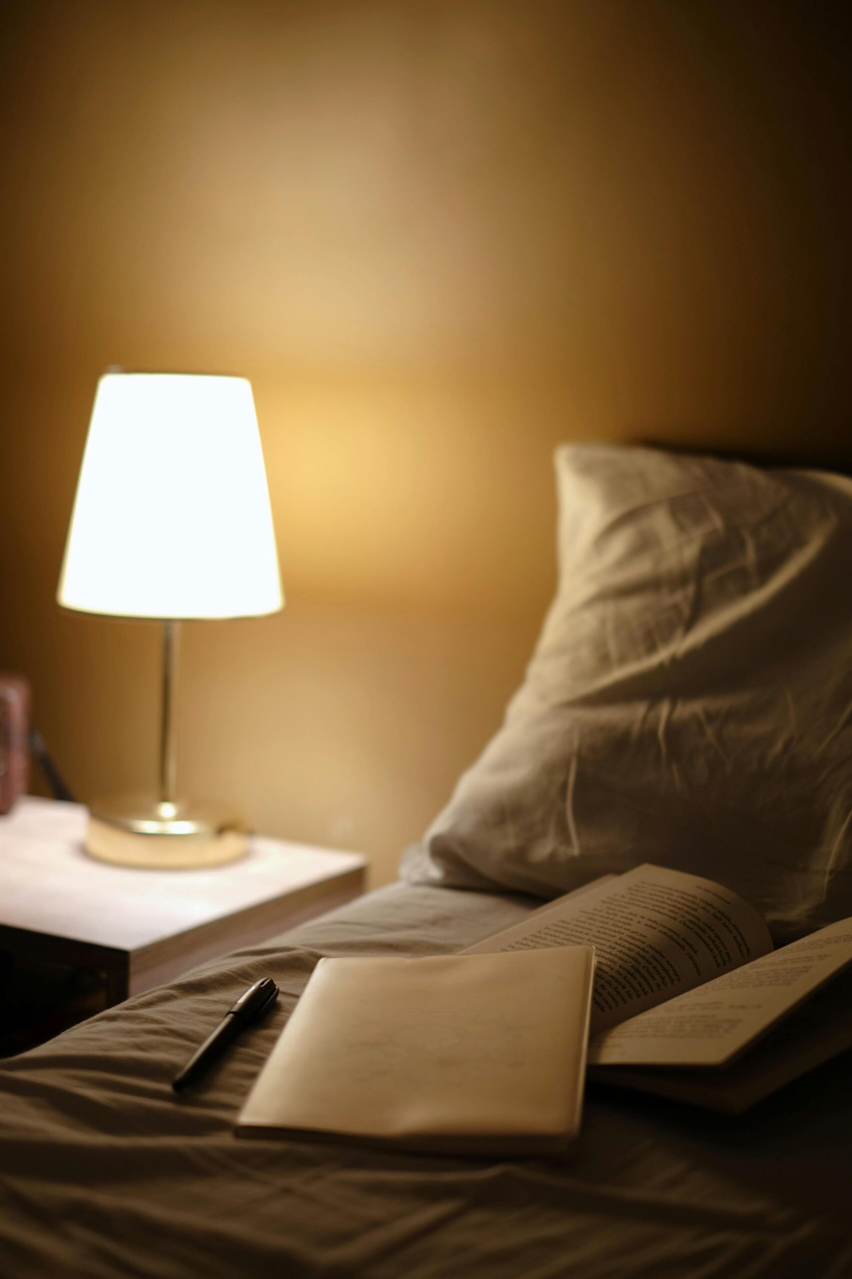 A softly lit bedroom with an open notebook resting on a bed beside a warm bedside lamp, symbolizing rest, winding down, and the supportive practices taught in sleep hygiene presentations at The Mindful Place in Ontario.
